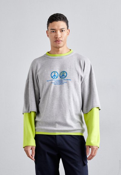 Gray oversized sweater with short sleeves and a green inner layer. Features two peace symbols and colorful text on the front.