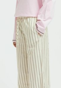 Striped wide-leg trousers in cream with brown vertical lines, made of a smooth fabric. Features an elastic waistband and side pockets.
