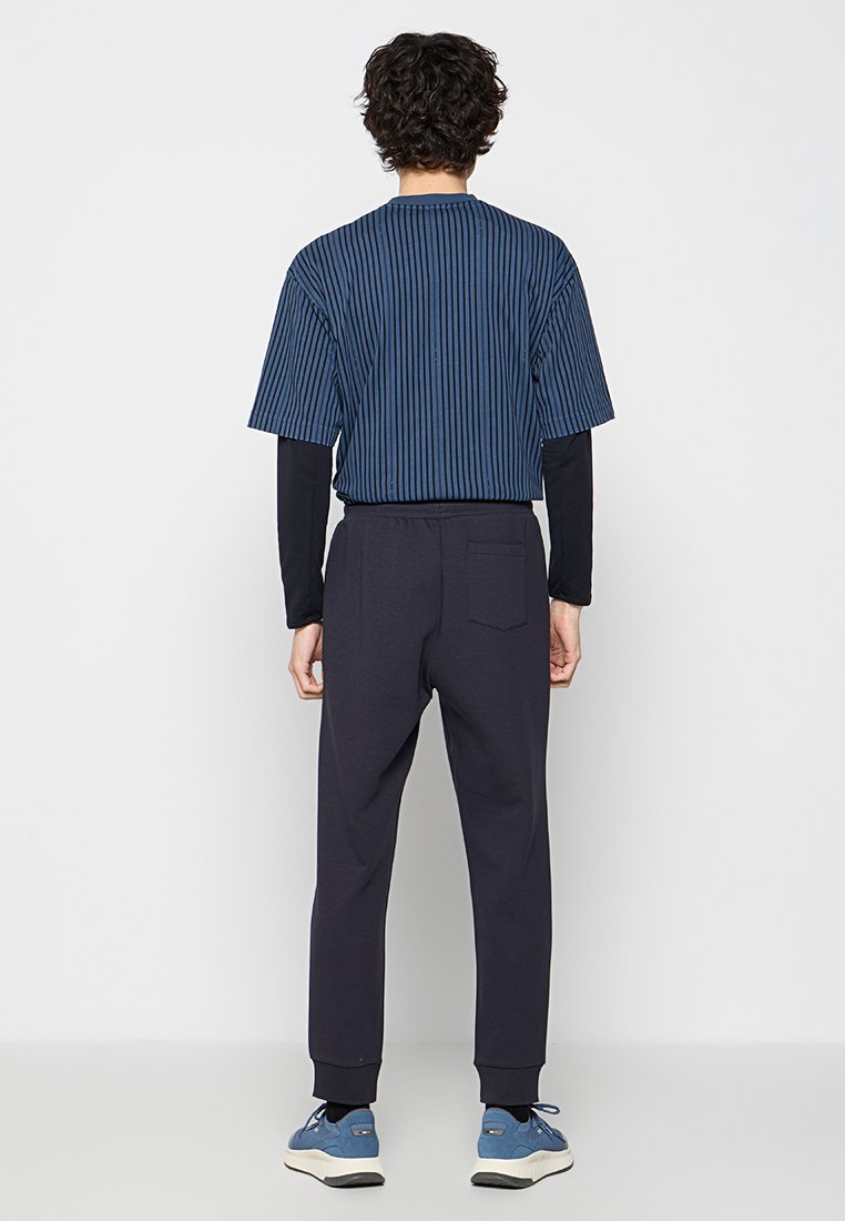 Marineblauw en gestreept T-shirt met korte mouwen, gecombineerd met marineblauwe joggers met elastische taille. Schoenen zijn blauw met beige zolen. Minimalistisch ontwerp, relaxed fit.