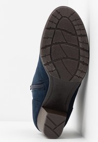 Semelle d’une botte en daim bleu foncé avec fermeture éclair latérale, montrant un motif de semelle détaillé et un petit talon bloc sur fond blanc.