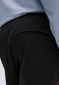 Schwarze Jogginghosen aus weichem Stoff verfügen über eine Reißverschlusstasche auf der Rückseite und einen glatten, elastischen Bund, kombiniert mit einem hellblauen Oberteil.