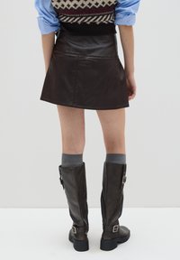 Bruine leren mini-jurk met zichtbare naden, gecombineerd met bruin boven de knie laarzen en grijze sokken, tegen een eenvoudige witte achtergrond.