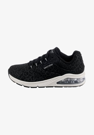 Chaussure de sport noire Skechers avec imprimé léopard subtil, lacets noirs, semelle intermédiaire blanche et semelle à coussin d’air transparente sur fond blanc.