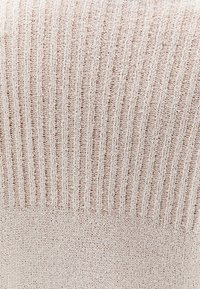 Helles beige, geripptes Strickgewebe mit einer weichen Textur. Das Design zeigt abwechselnde vertikale Streifen und einen glatten unteren Abschnitt.
