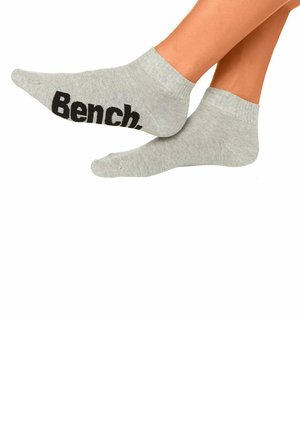 Feet wearing light gray ankle socks, one sock showing the black "Bench." logo on the sole against a white background.