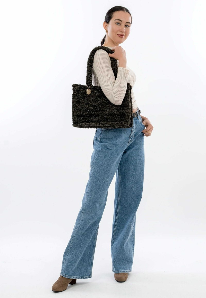 Svart vävd tote-väska med strukturerad yta och stadiga handtag. Modellen bär en ljusfärgad långärmad topp och högmidjade blåjeans.
