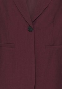 Blazer bordeaux foncé à revers crantés, fermeture par un bouton noir et deux poches horizontales à l'avant.