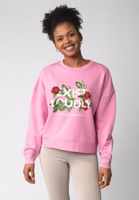 Roze sweatshirt met een ronde hals. Voorzijde met bloemmotief en tekst "EXIST LOUDLY." Geribbelde manchetten en zoom. Combineer met licht geribbelde leggings.