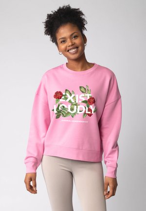 Roze sweatshirt met een ronde hals. Voorzijde met bloemmotief en tekst "EXIST LOUDLY." Geribbelde manchetten en zoom. Combineer met licht geribbelde leggings.