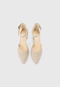 Chaussures à talons hauts en daim beige avec un bout pointu, une bride de cheville avec une boucle en argent et un talon modéré. Doublure intérieure lisse.