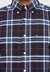 Camicia a quadri blu, rossa e bianca, con bottoni e realizzata in cotone, caratterizzata da un colletto, chiusura con bottoni e una tasca sul petto con un piccolo logo.