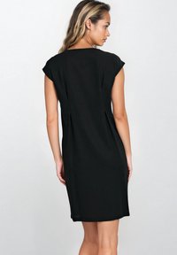 Czarna sukienka z krótkim rękawem o luźnym kroju, sięgająca do kolan, o gładkiej strukturze i z bocznymi rozcięciami dla swobody ruchów.