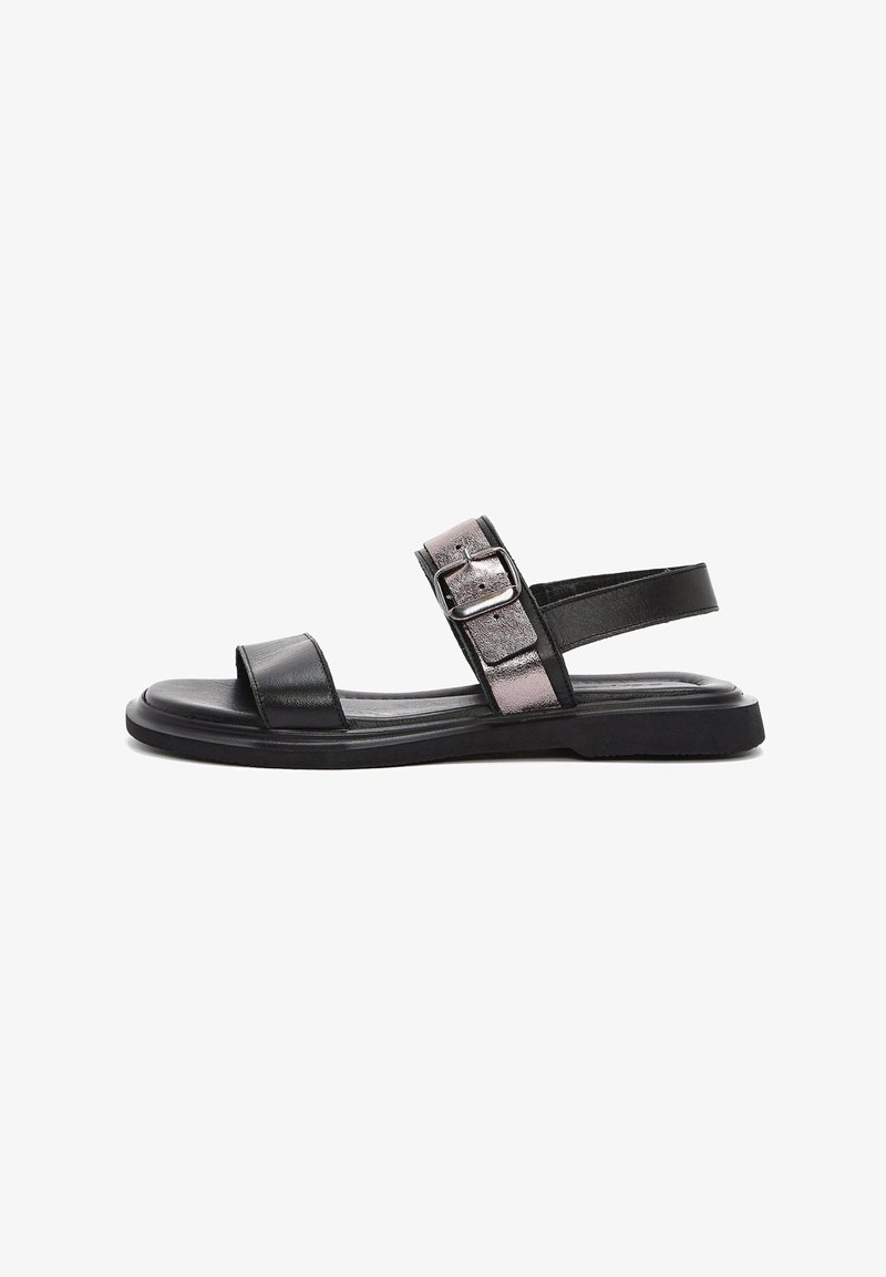 Sandalia de cuero negro con una tira delantera ancha, hebilla metálica ajustable y suela plana. Presenta una textura suave y un diseño minimalista.