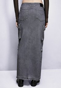 Gonna in denim grigio lungo con tasche cargo, orlo sfrangiato e vita aderente. La texture è robusta con una finitura liscia.