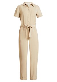 Combinaison en lin beige avec des manches courtes, un col et une poche avant. Possède une taille ceinturée et des jambes fuselées avec des poignets retroussés.