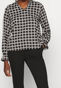 Fließende Bluse in Schwarz-Weiß mit Karomuster, V-Ausschnitt und gerafften Bündchen. Hergestellt aus leichtem Stoff, lockere Passform für optimalen Komfort.