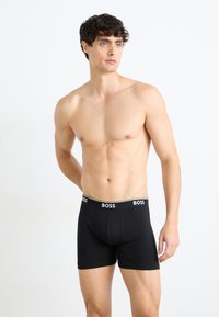Schwarze Boxershorts mit elastischem Bund, der das Logo "BOSS" in Weiß zeigt. Glattes Gewebe, figurbetontes Design, mittellange Oberschenkel.