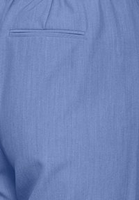 Tessuto blu con una sottile texture, dotato di una tasca posteriore. Il materiale sembra leggero e liscio, adatto per un abbigliamento informale.