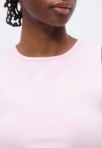 Κοντινή λήψη ενός ατόμου που φοράει ανοιχτό ροζ αμάνικο τοπ Nike με το λευκό λογότυπο Nike swoosh τοποθετημένο στο κέντρο κάτω από την γραμμή του λαιμού.