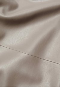 Tessuto in similpelle beige con una finitura morbida e testurizzata. La superficie mostra una leggera lucentezza e pieghe delicate per una caduta naturale.