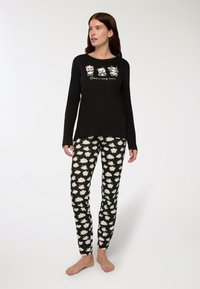 Pigiama con maniche lunghe di colore nero, decorato con animali dei cartoni animati e testo. Pantaloni neri con motivo a nuvole bianche. Tessuto morbido, vestibilità rilassata, design minimal.