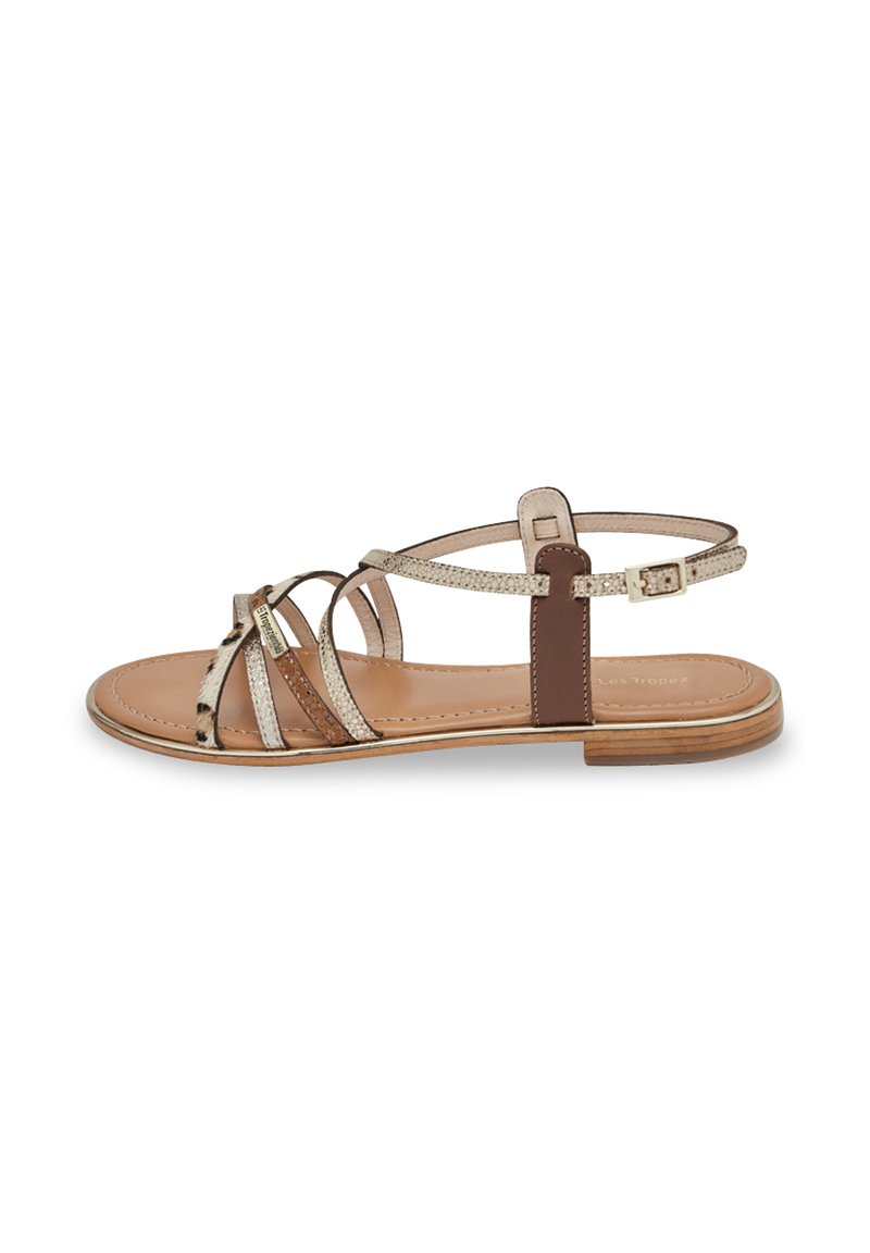 Brown leather sandal with metallic cross straps, flat sole, and adjustable ankle buckle. Smooth texture and minimalist design.