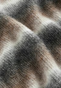 Tissu en laine douce à motif rayé dans des tons gris, beige et blanc, montrant un gros plan de sa surface tricotée texturée.