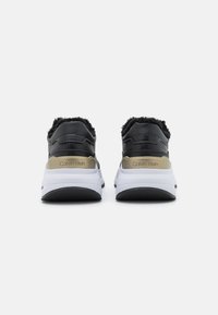 Svarta och guldiga träningsskor med en texturerad baksida, utrustade med en mjuk kant, vit mellansula och svart gummisul. Logotyp synlig.