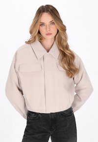 Lichtbeige fleecedonker met een kraag, twee voorzakken en een cropped ontwerp. Gladde textuur en zichtbare stikdetails.