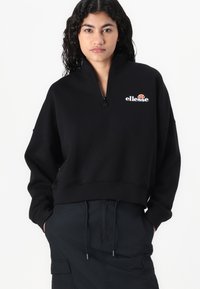 Felpa zip nera con colletto alto e vestibilità ampia. Caratterizzata da un logo "ellesse" bianco sul petto e polsini a coste. Texture opaca.