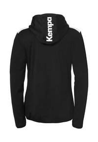 Veste à capuche noire avec des manches longues, présentant des accents blancs sur les épaules et un grand logo "Kempa" à l'arrière. Tissu doux et lisse.