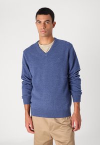 Niebieski sweter w serek, wykonany z miękkiego materiału. Posiada ściągacze przy rękawach i u dołu, zestawiony z beżowym t-shirtem, z subtelnym detalem z logo.