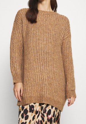 Woman wearing a chunky, camel-colored knit sweater over a beige skirt with black and brown animal print pattern.