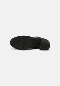 Black footwear with a textured rubber sole featuring a rugged tread pattern. The design is smooth with a slightly elevated heel.