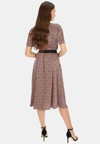 Kwiatowa sukienka midi z krótkimi rękawami, czarnym paskiem w talii, materiał chiffon, różowe i fioletowe wzory, rozkloszowany dół, w komplecie z czarnymi sandałami na obcasie.