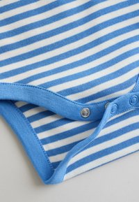 Tkanina plavih i bijelih prugastih dječjih bodija s plavim rubom i metalnim dugmadima na pritisak djelomično otvorenim na svijetloj podlozi.