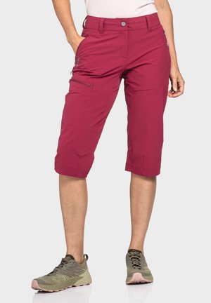 Knielange bordeauxrote Shorts aus leichtem Stoff, mit Reißverschlusstaschen und tailliertem Schnitt, kombiniert mit olivgrünen Sneakers.