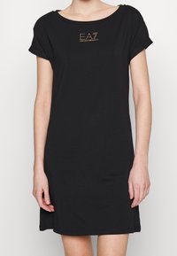 Czarna sukienka T-shirt z miękkiej bawełny, z krótkimi, podwiniętymi rękawami i okrągłym dekoltem. Złota naszywka z logo na klatce piersiowej.