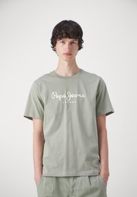 Camiseta de algodón verde oliva con mangas cortas, que presenta el logotipo en blanco de "Pepe Jeans" y el texto "LONDON". Diseño simple y de corte relajado.
