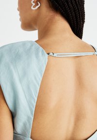 Robe en lin bleu clair avec un dos décolleté et un détail discret aux épaules. Présente une fermeture éclair noire avec un petit crochet.