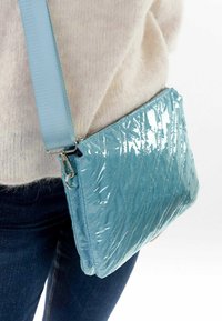 Bolsa azul acolchada con un acabado brillante, que presenta una correa de hombro y herrajes plateados. Textura suave con un patrón de costura diagonal.