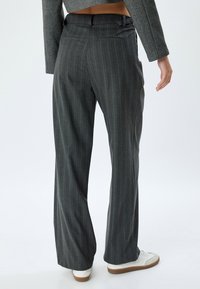 Pantalones gris de raya diplomática con un corte de pierna ancha, que presentan un detalle de cinturón y bolsillos traseros, combinados con zapatillas blancas. Textura de tela suave.