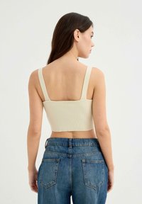 Top corto de color crema con textura acanalada y tirantes anchos, combinado con jeans de mezclilla azul de tiro alto. La tela tiene una textura suave.