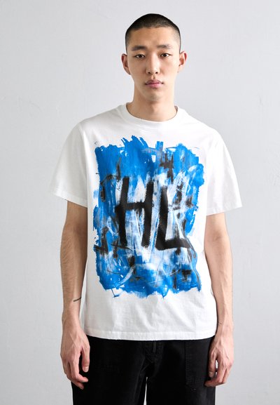 T-shirt blanc à manches courtes avec un design abstrait de peinture bleue et noire, portant le logo "HL" affiché en évidence sur le devant.