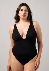 Svart baddräkt med djup V-ringning, breda axelband, sl ät textur och hög skärning på benen som framhäver en smickrande silhuett.