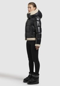 Sort dunjakke med krave og kant i faux shearling, har lynlås foran, to sidelommer og en blank finish. Bæret sammen med sorte tights og støvler.
