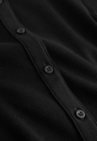 Gilet noir côtelé avec une rangée de boutons noirs sur le devant. Texture lisse avec une coupe structurée.