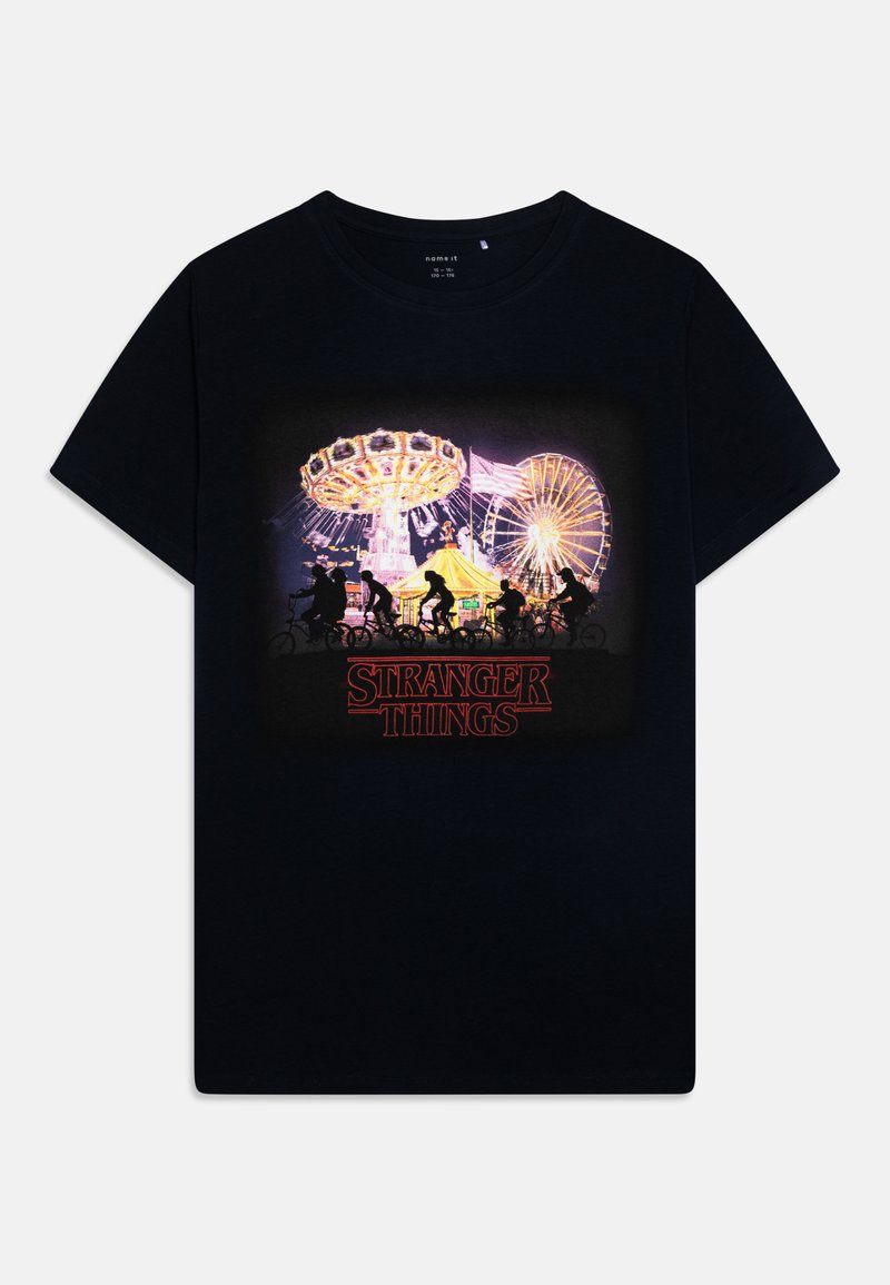 Juodas medvilninis marškinėliai su spalvinga karnavalo scena ir užrašu "STRANGER THINGS" raudona spalva, trumpomis rankovėmis ir apvalia apykakle.