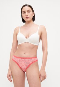 Hvit polstret bh med tynne stropper, kombinert med rosa mønstrede truser med korallfarget kant og en teksturert design.