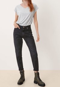 Szara koszulka z dekoltem w serek i podwiniętymi rękawami, zestawiona z czarnymi jeansami z wysokim stanem oraz oliwkowozielonymi botkami na sznurowadła. Gładka tkanina, dopasowany krój.